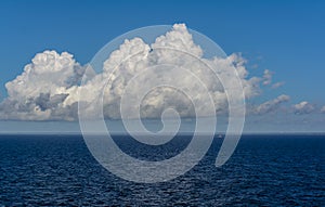 White cumulus clouds in sky over blue Baltic sea water landscape, with vague silhouette of Finland in the horizon