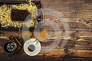 White cup with black coffee and coffee grains on a wooden table background. View from above. Place for text.