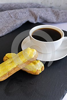 A white cup with black coffee and lemon eclairs on the table. Confectionery for sweet tooth.