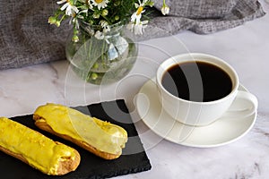 A white cup with black coffee and lemon eclairs on the table. Confectionery for sweet tooth.