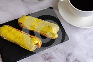 A white cup with black coffee and lemon eclairs on the table. Confectionery for sweet tooth.