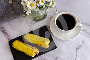 A white cup with black coffee and lemon eclairs on the table. Confectionery for sweet tooth.