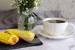 A white cup with black coffee and lemon eclairs on the table. Confectionery for sweet tooth.