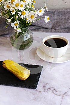 A white cup with black coffee and lemon eclairs on the table. Confectionery for sweet tooth.