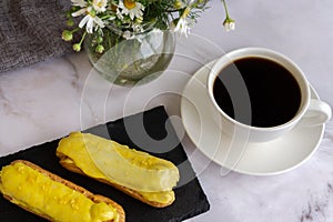 A white cup with black coffee and lemon eclairs on the table. Confectionery for sweet tooth.