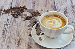 White cup with black coffee with milk. Handful of coffee beans on a wooden table. horizontal view of a cup with a coffee drink.