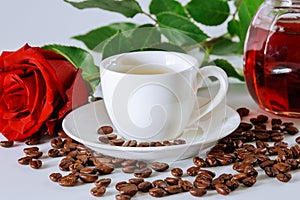 White cup of black coffee with a red rose and coffee beans scattered on a white table