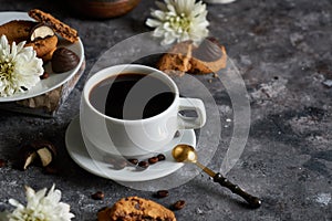 White cup of black strong coffee with coffee beans and cookies on dark background