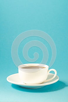 white cup on a blue background/white cup with a saucer full of black coffee on a blue background with copyspace