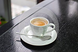 White Cup of cappuccino or expresso coffee with foam on the table in a cafe or restaurant with a shiny spoon
