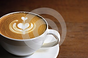 White cup of cappuccino with latte art on wooden background at coffee cafe