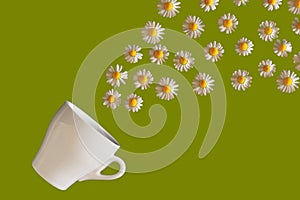 White cup and chamomile flowers on a green background. Chamomiles come out of the cup like steam. Chamomile tea concept. Flat lay