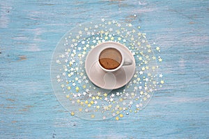 A white cup of christmas coffee among golden starlets on a wooden azure background, table, top view