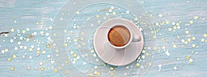 A white cup of christmas coffee among golden starlets on a wooden azure background, table, top view, baner