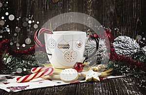 White cup with Christmas decoration on table with lollipops, cookies, Christmas balls and Christmas tree branches.