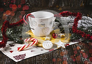 White cup with Christmas decoration on table with lollipops, cookies, Christmas balls and Christmas tree branches.