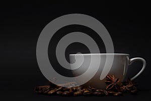 White cup, coffee beans, anise, cinnamon sticks on black background