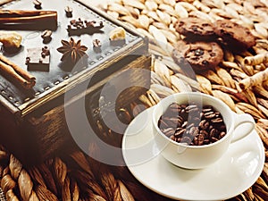 White cup with coffee beans and chocolate chip cookies on a wicker background.