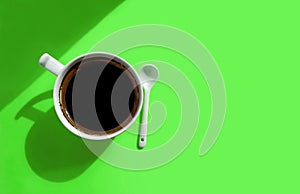 White cup of coffee and white ceramic spoon on a lime green background