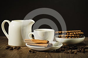 white cup of coffee with cinnamon, creamer and cookies/white cup of coffee with cinnamon, creamer and cookies on a wooden table.