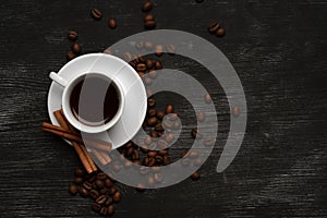 White cup with coffee cinnamon sticks on a black background with coffee beans and place for text top view