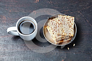 White cup with coffee and crunchy crispbread in a metal bowl on a wooden background, closeup