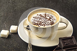 White cup of coffee with dark chocolate on black background.