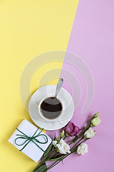 white cup with coffee and flowers and a gift on a yellow-pink background with a copy of the space, flat layout, top view