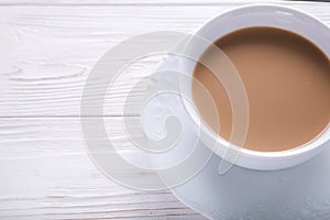 White cup of coffee with milk or tea with milk on white wooden background decorated with coffee beans.