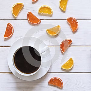 White cup of coffee and multi-colored fruit marmalade on a white wooden table