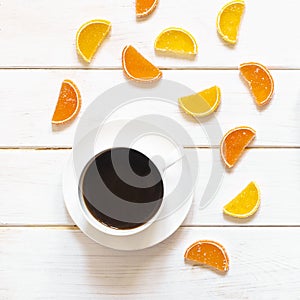 White cup of coffee and multi-colored fruit marmalade on a white wooden table