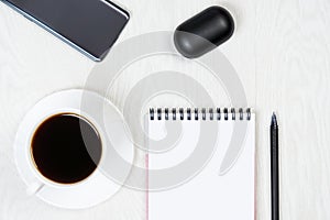 White cup of coffee, notebook, pen, phone, headphones on a white table