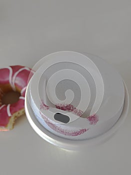 White cup of coffee with red lipstick mark and flower-like pink doughnut