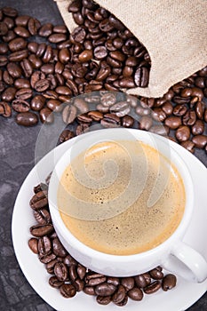 White cup of coffee and roasted fragrant dark coffee grains in bag