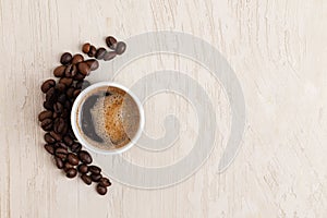 White cup of coffee and smile made of roasted coffee beans on light coloured wooden table