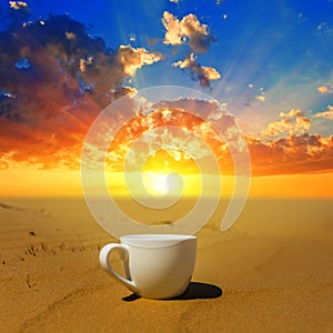 white cup of coffee stay on sand at the dramatic sunset