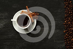 White cup with coffee sticks of cinnamon anise on a black background with coffee beans and place for text