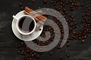 White cup with coffee sticks of cinnamon and anise on a black background with coffee beans and place for text top view