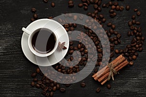 White cup with coffee sticks of cinnamon and anise on a black background with coffee beans and place for text top view