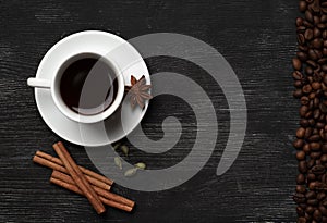 White cup with coffee sticks of cinnamon green cardamom and anise on a black background with coffee beans and place for text top