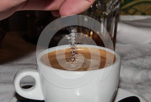 White Cup of coffee. Sugar is poured into the coffee drink