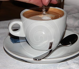 White Cup of coffee. Sugar is poured into the coffee drink