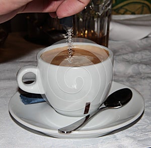 White Cup of coffee. Sugar is poured into the coffee drink