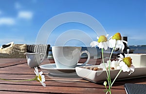 White cup coffee on table and daisy flowers on beach cafe at sea blue sky summer morning day scenery