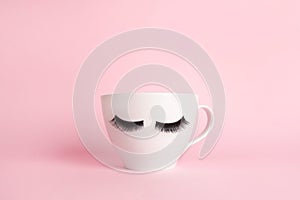 White cup coffee or tea mug with false lashes on a pink background. Morning energy. Female cute background