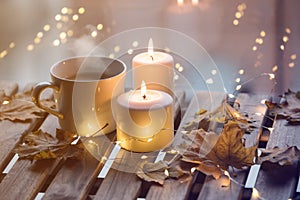 White cup of coffee or tea near candles with maple leaves