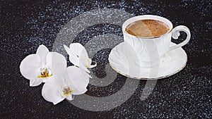 White cup of coffee and white orchid flowers. Romantic composition in white on a black background