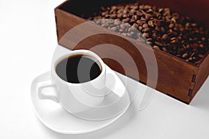 White cup of coffee on a white saucer, natural wooden box with coffee beans on a white background, isolate, angle view from above