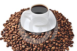 White cup of coffee on a white saucer stands on a hill of coffee beans on a white background  angle view from above