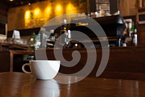 White cup of coffee on wooden bar in Coffee shop blur background